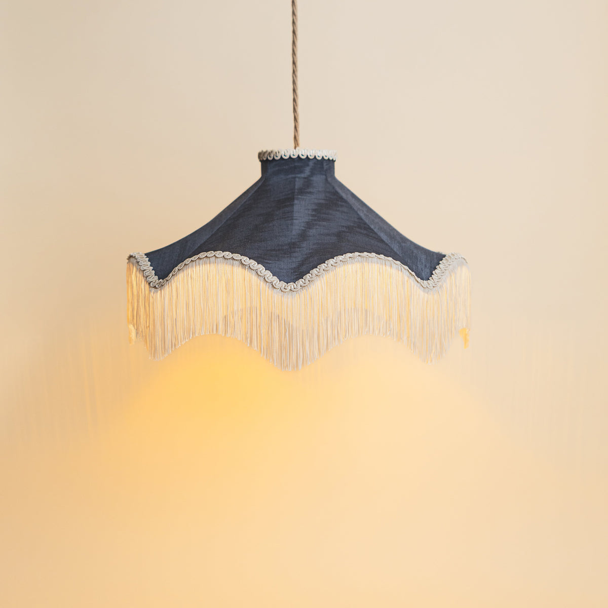 The Daisy Moiré Midnight lampshade lit as a ceiling pendant against a warm cream wall