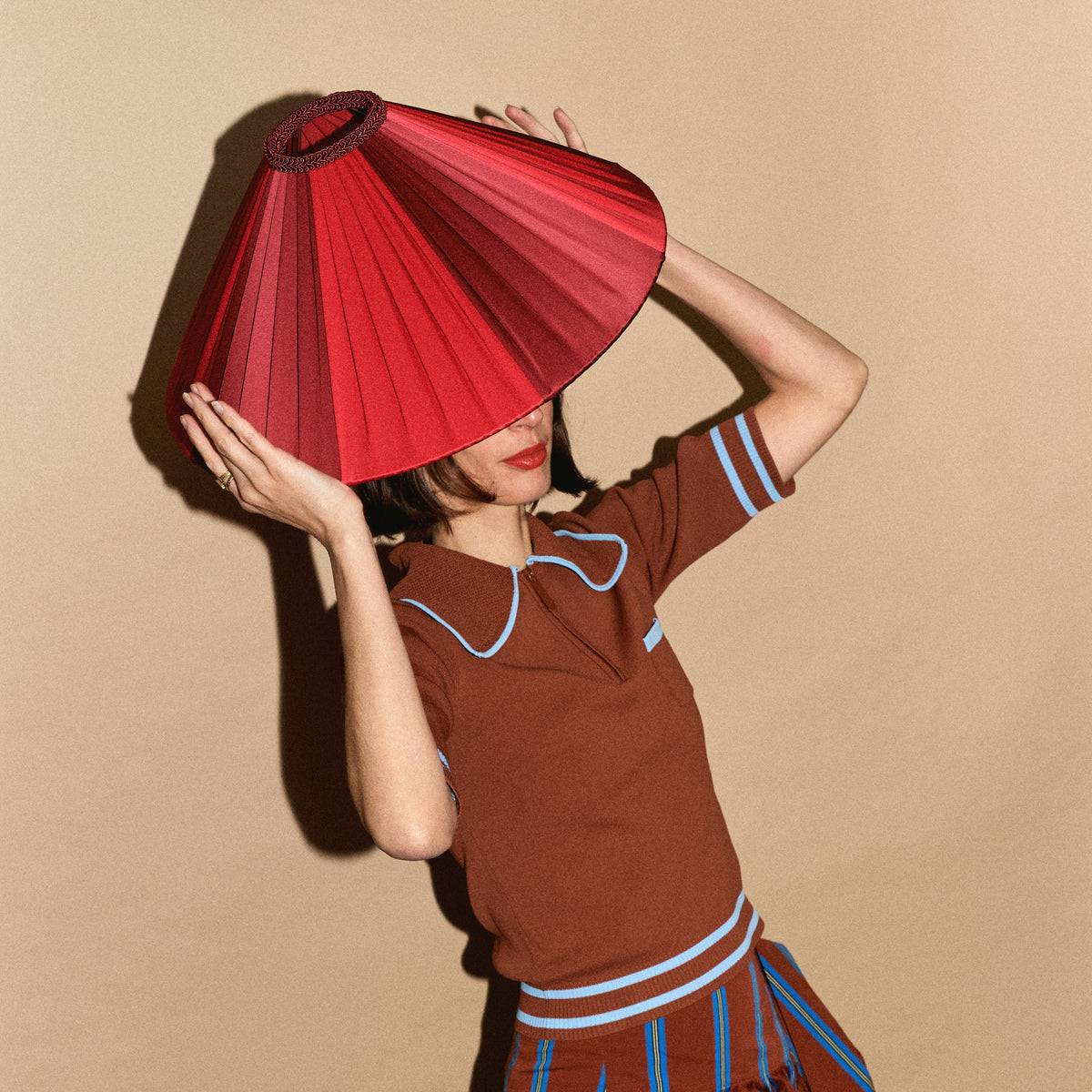 A model in a brown collared top holding the Fitz Burgundy pleated silk lampshade over her head