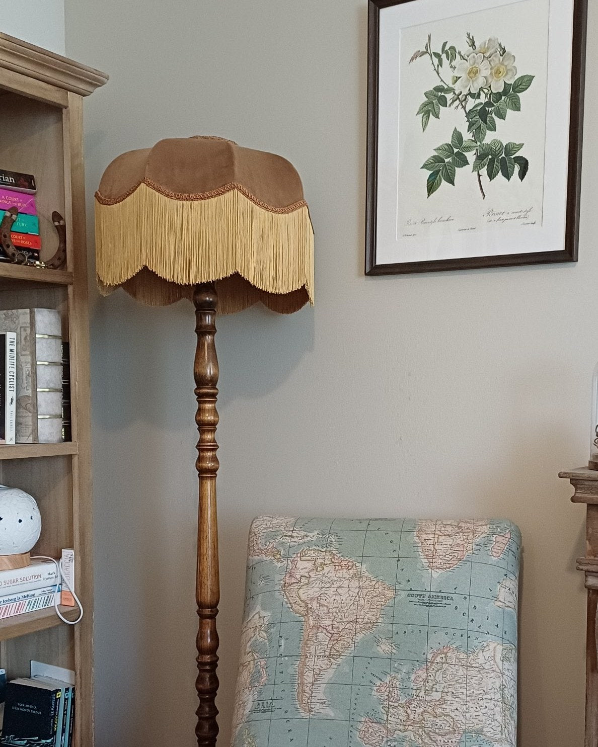 Brown velvet fringed floor lamp shade beside a map-print armchair