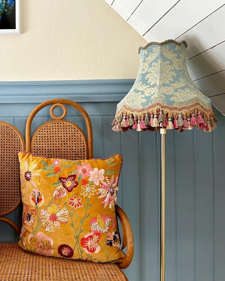 Blue damask lampshade with tassel trim beside a cane bench