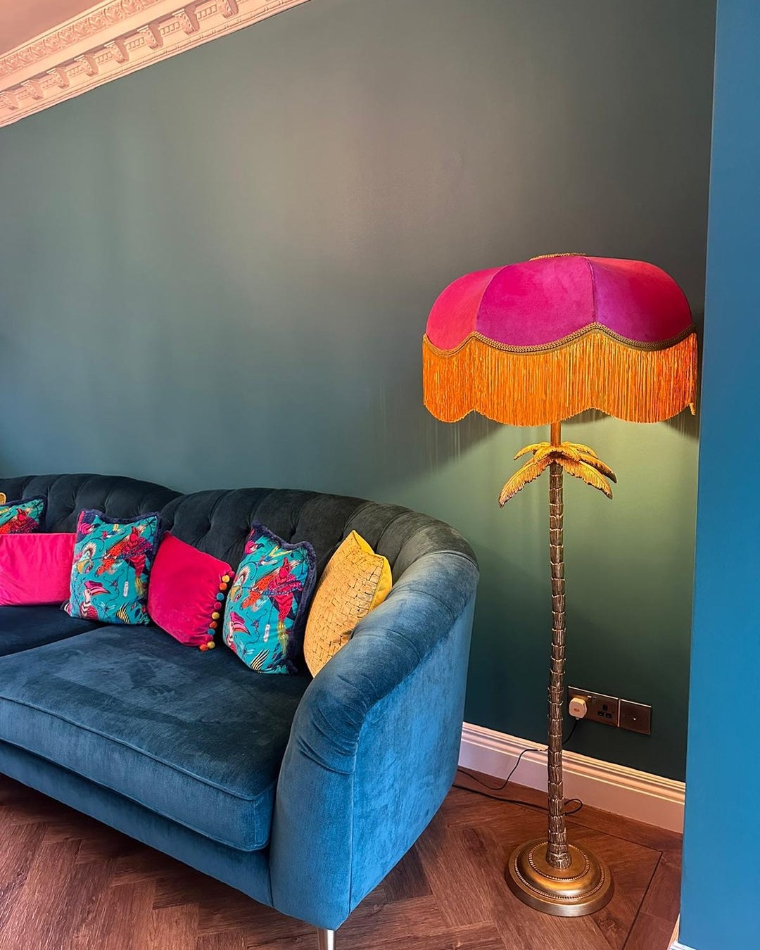 Pink velvet fringed shade on a gold palm floor lamp against a teal wall