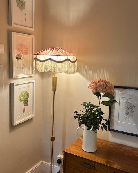 Pink fringed floor lamp beside botanical prints
