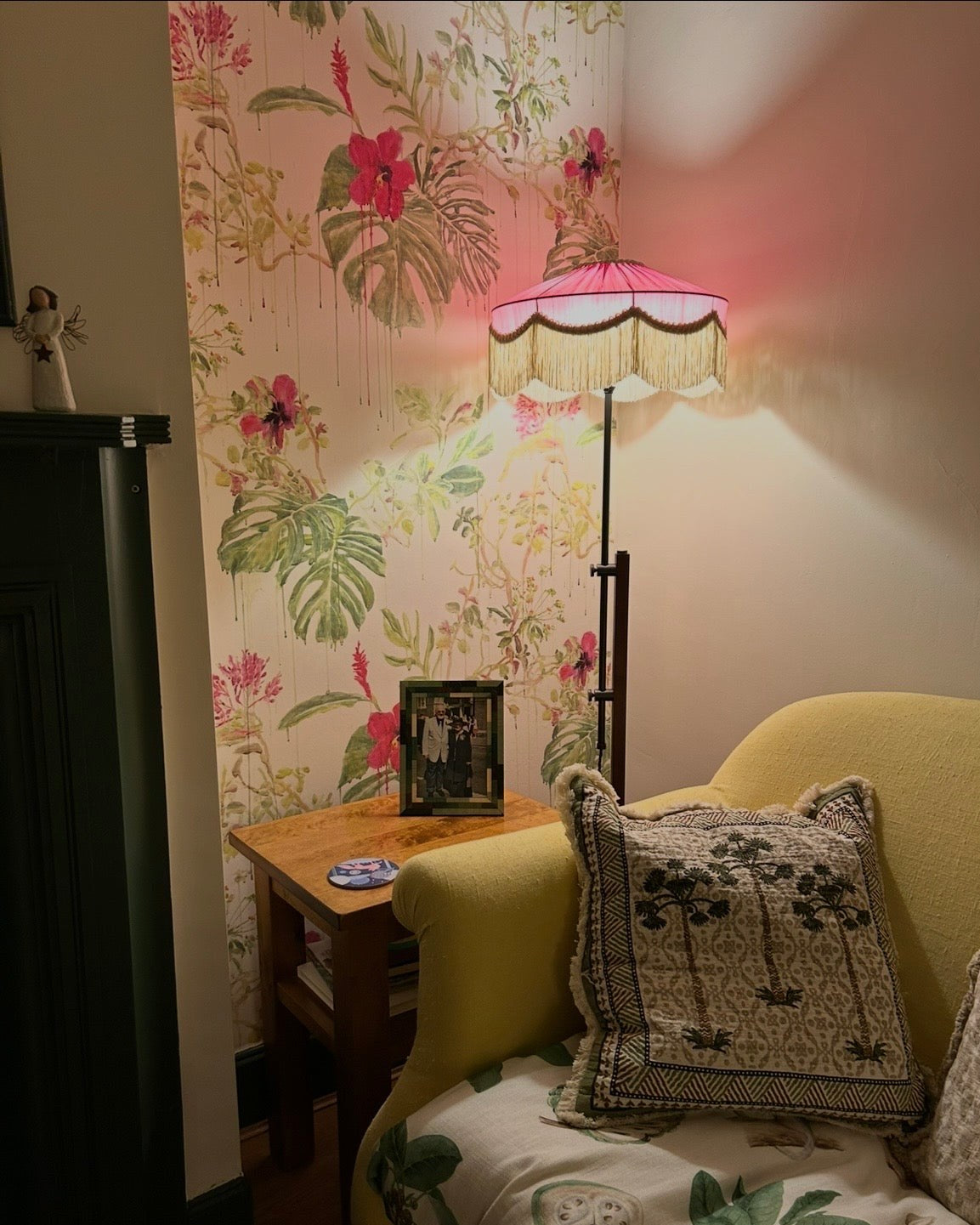 Pink fringed floor lamp glowing against tropical wallpaper