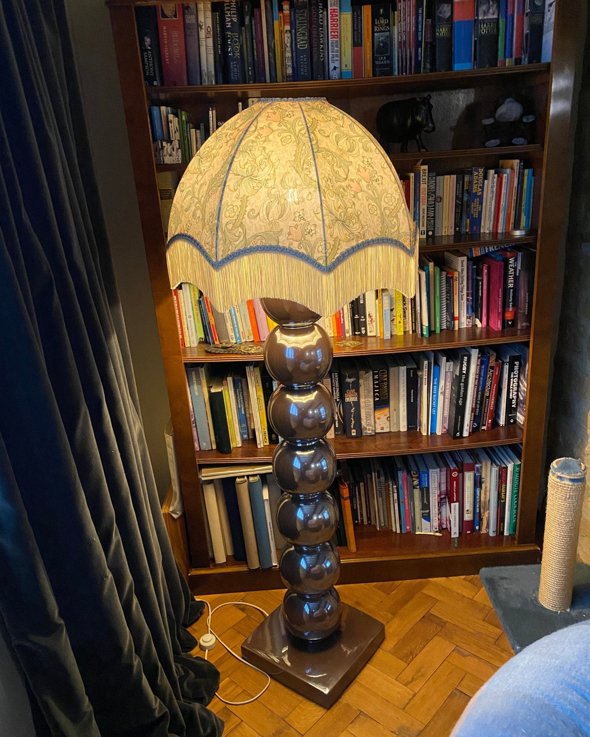 William Morris print dome lampshade with fringe in front of a bookcase