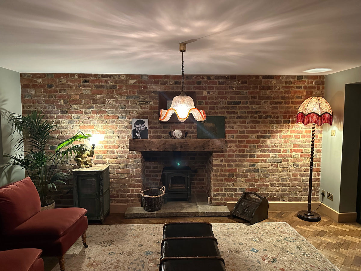 Patterned fringed floor lamp shade beside an exposed brick fireplace