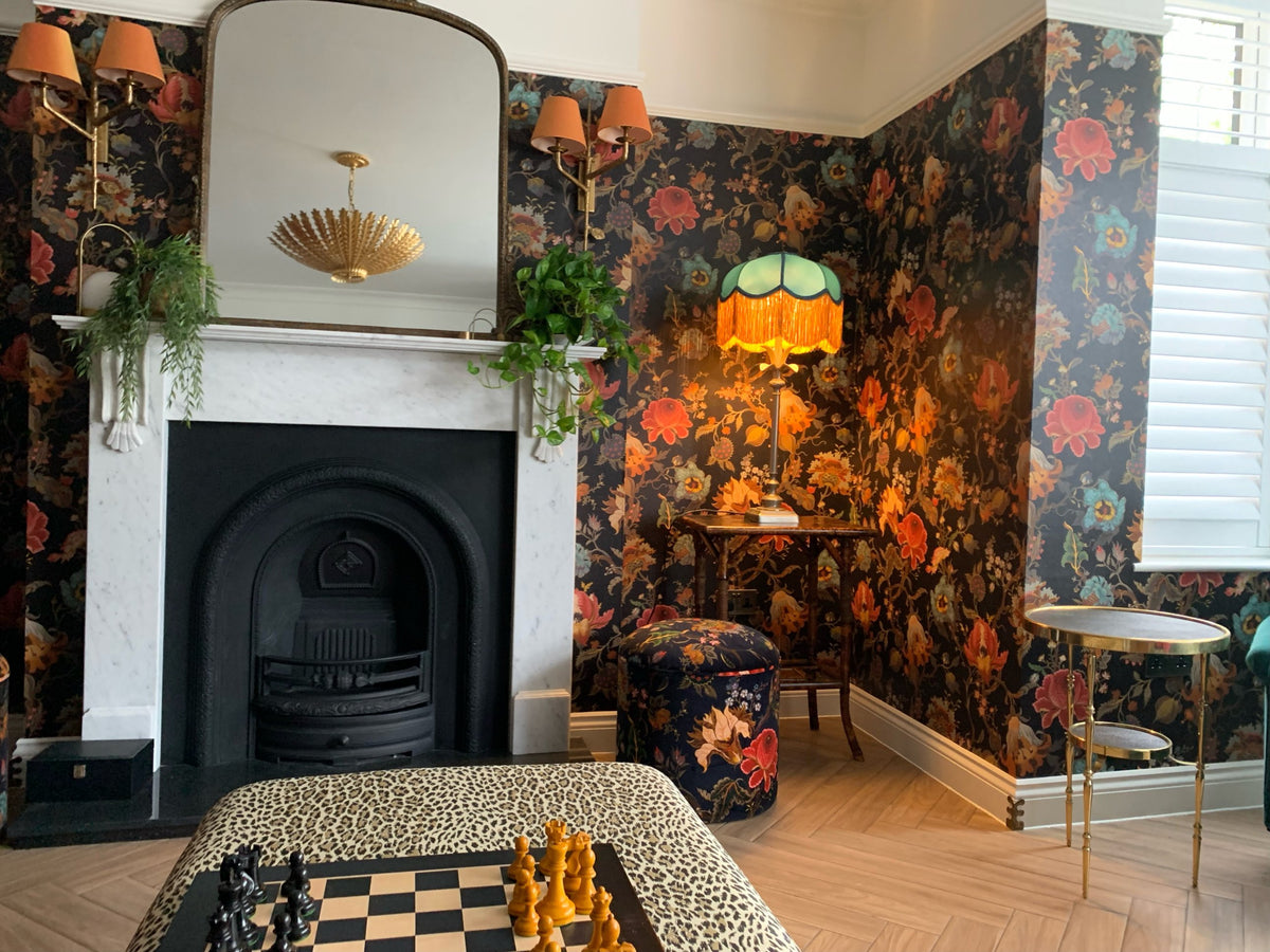 Green fringed table lamp glowing against dark floral wallpaper