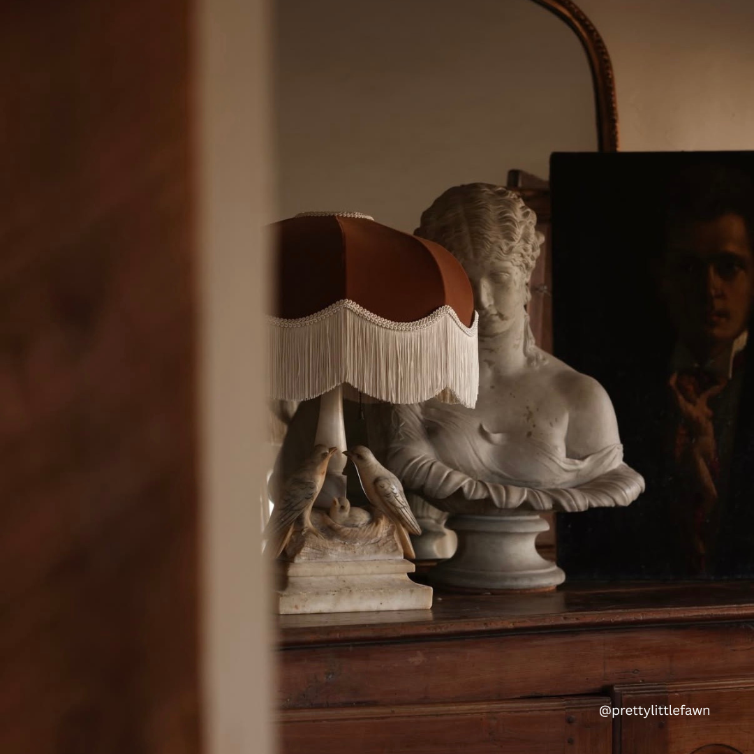 The Emmy brown velvet lampshade with ivory fringe on a wooden sideboard beside a classical marble bust (@prettylittlefawn)
